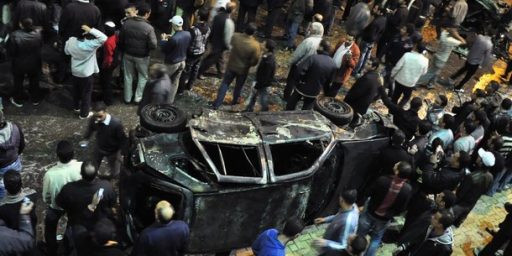 Onlookers gather around a damaged car after a bomb exploded in Alexandria
