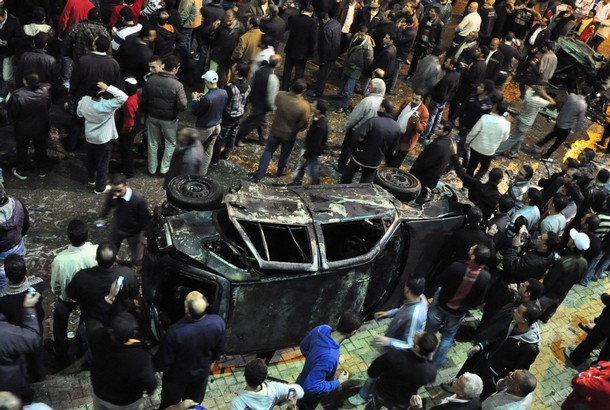 Onlookers gather around a damaged car after a bomb exploded in Alexandria