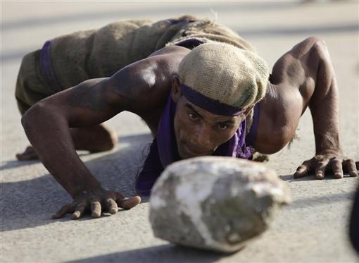 A Cuban sackcloth-dressed worshipper crawls as he pushes a rock to pay homage along a road leading to the shrine of Saint Lazarus in the town of Rincon near Havana