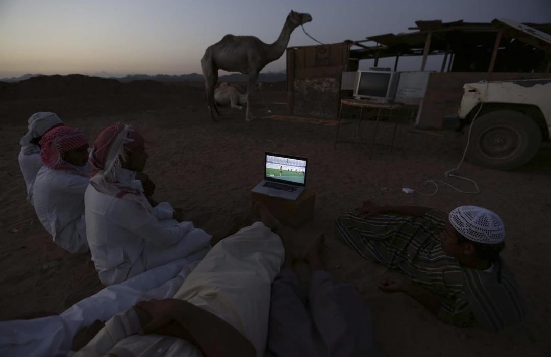 Men watch the 2014 World Cup Group B soccer match between the Netherlands and Australia on a laptop, at a camel market in Daba