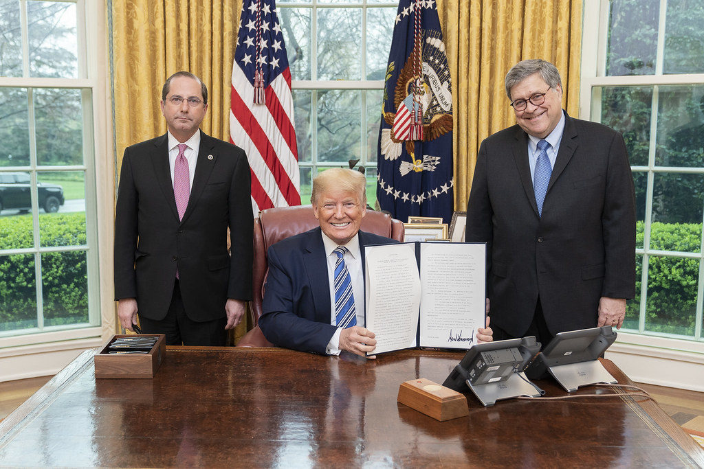 President Donald J. Trump, joined by Health and Human Services Secretary Alex Azar, left, and Attorney General William Barr, displays his signature after signing an Executive Order to Prevent Hoarding and Price Gouging, Monday, March 23, 2020, in the Oval Office of the White House. (Official White House Photo by Shealah Craighead)